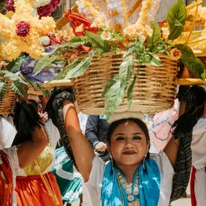 A woman in traditional Oaxacan dress carrying a flower-filled basket during a festival.
