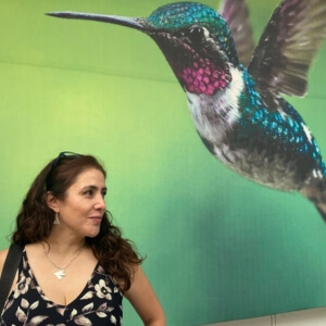 Portrait of Lorena, Mexico Travel Concierge, posing in front of a vibrant hummingbird mural in Puebla, Mexico.