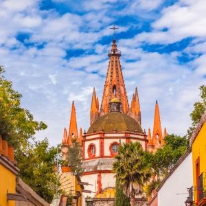 A San Miguel de Allende cobblestone street with the San Miguel Church in the background and a group of tourists looking at it