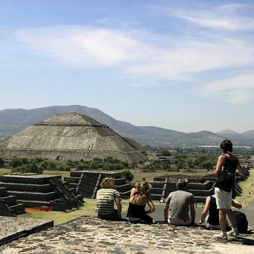 Small group sitting on a stone platform overlooking the Sun Pyramid at Teotihuacan archaeological site.
