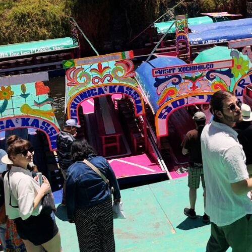 Colorful trajinera boats at Xochimilco canals with travelers getting ready for a private boat tour.