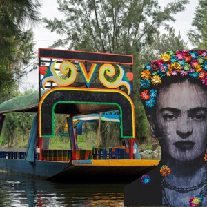 A traditional colorful trajinera boat in Xochimilco next to a large Frida Kahlo art installation.