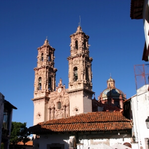 Santa Prisca Church towers and colonial architecture in Taxco, Mexico, under a clear blue sky.